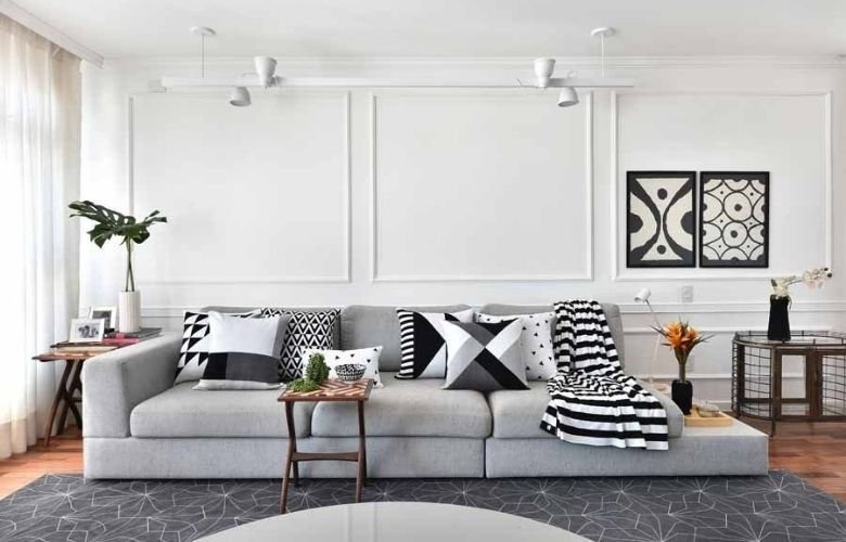 Trico decor em almofadas para a sala de estar com criado mudo e objetos decorativos, quadros e vasos de flores, tapete cinza