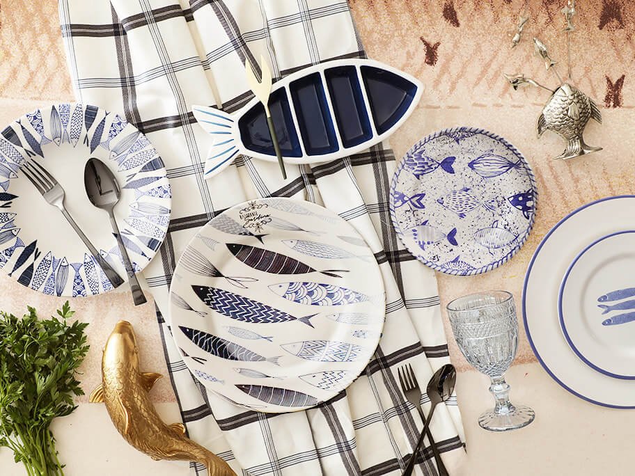 pratos estampados com peixes e decoração navy em azul e toalha de mesa xadrez, taça de vidro e talheres pretos