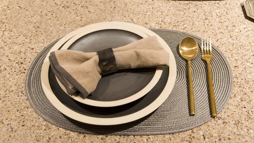Mesa posta em tons terrosos, jogo americano cinza, pratos marrons e talheres dourados