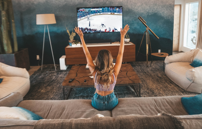 Foto de mulher sentada em um sofá grande com tv à frente em uma sala de cinema em casa.